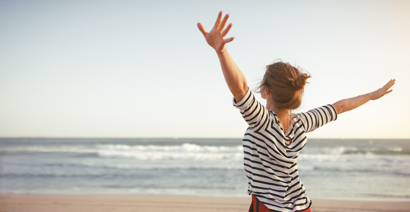 Μια γυναίκα στέκεται στην παραλία με τα χέρια της τεντωμένα